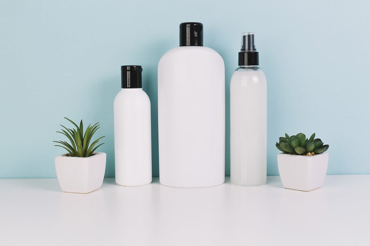 White cosmetic bottles for skincare routines arranged with green succulents on a white surface