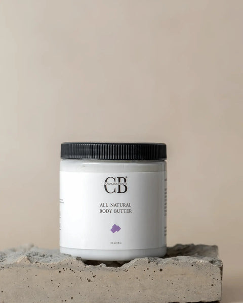 All natural body butter jar with black lid on a concrete block against a beige background