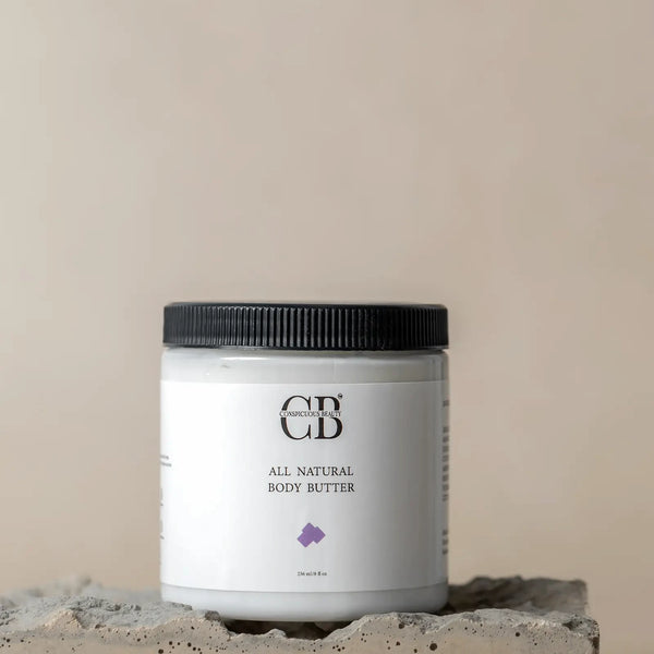 All natural body butter jar with black lid on a concrete block against a beige background